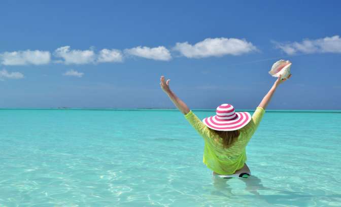 Een vrouw met zonnehoed in de zee bij de Bahamas